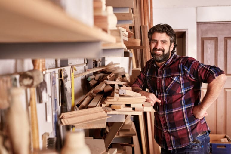 A smiling carpenter in red flannel standing in their workshop.