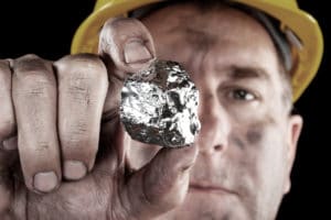 A closeup of a miner holding a silver nugget.