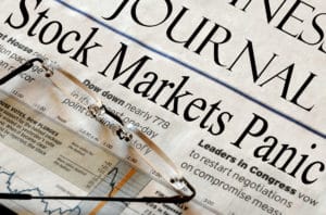 A closeup of glasses sitting on top of a newspaper with a headline that reads “Stock Markets Panic.”
