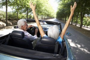 A retired couple driving in a convertible sports car.