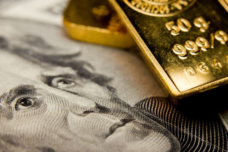 A closeup of gold bullions sitting on top of a U.S. banknote.