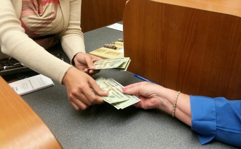 Womans hand reaches for money from teller at the bank for vacation cash and spending money.