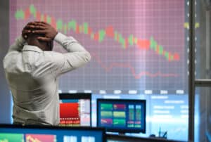 A trader with hands on his head, visibly stressed, stands in front of screens displaying falling stock market charts, symbolizing the impact of a black swan event on the financial markets.